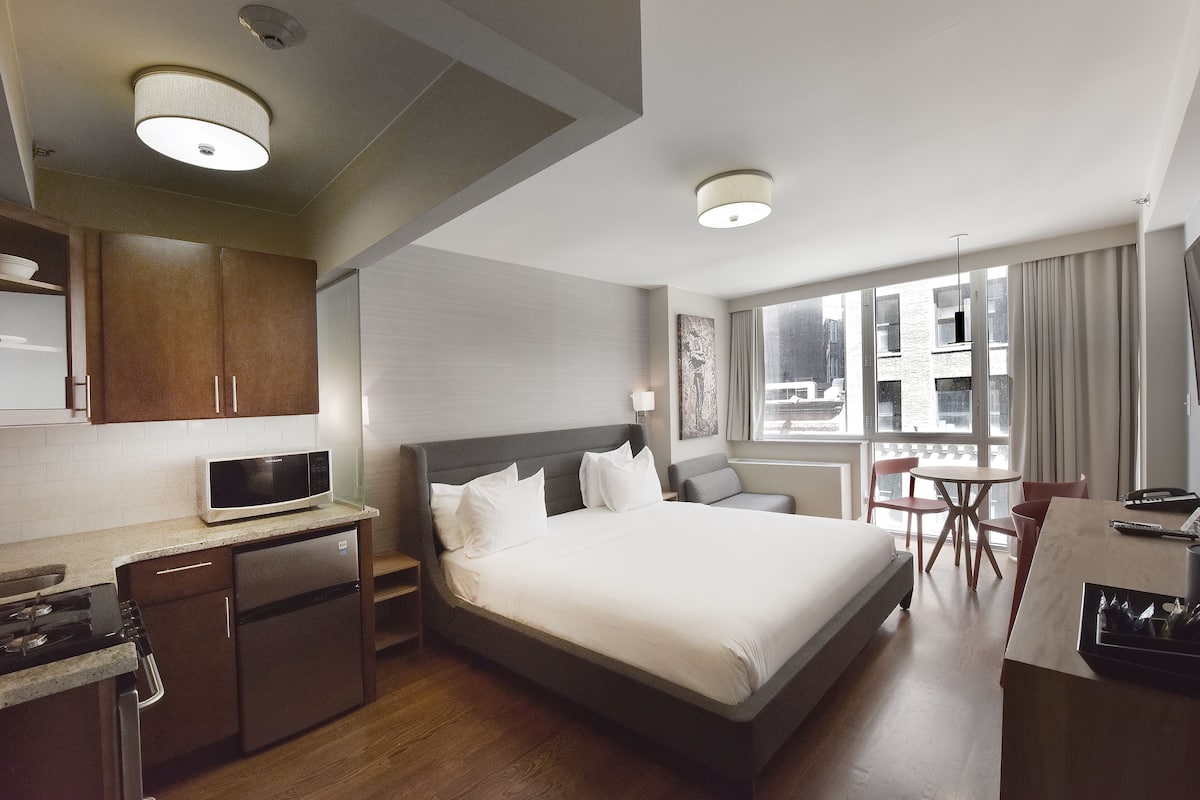 Habitación de hotel con cama, escritorio, microondas, refrigerador y ventana con cortinas.