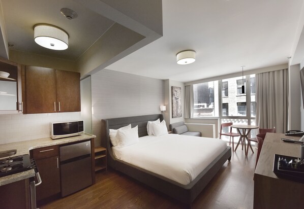 A hotel room with a bed, a desk, a microwave, a refrigerator, and a window with curtains.