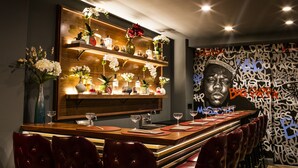 A bar area with a long counter, multiple shelves with bottles, and a wall with graffiti art. - Hotel 32 32 (New York)