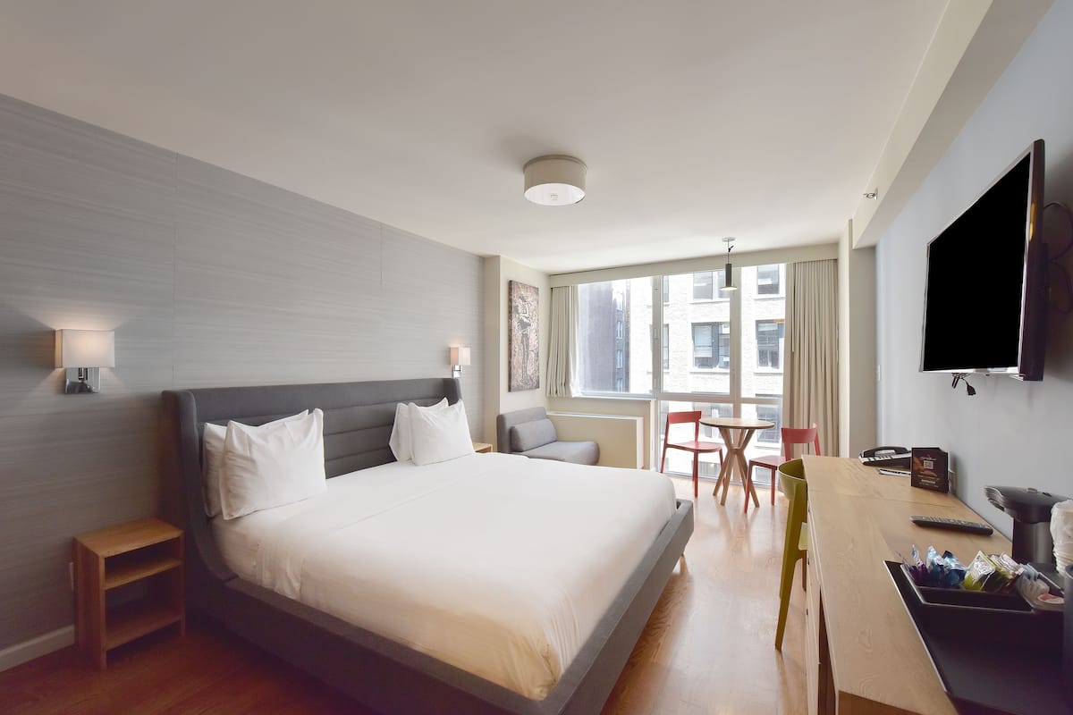Habitación de hotel con una cama grande, mesitas de noche, un escritorio con silla, televisor y una ventana con cortinas.