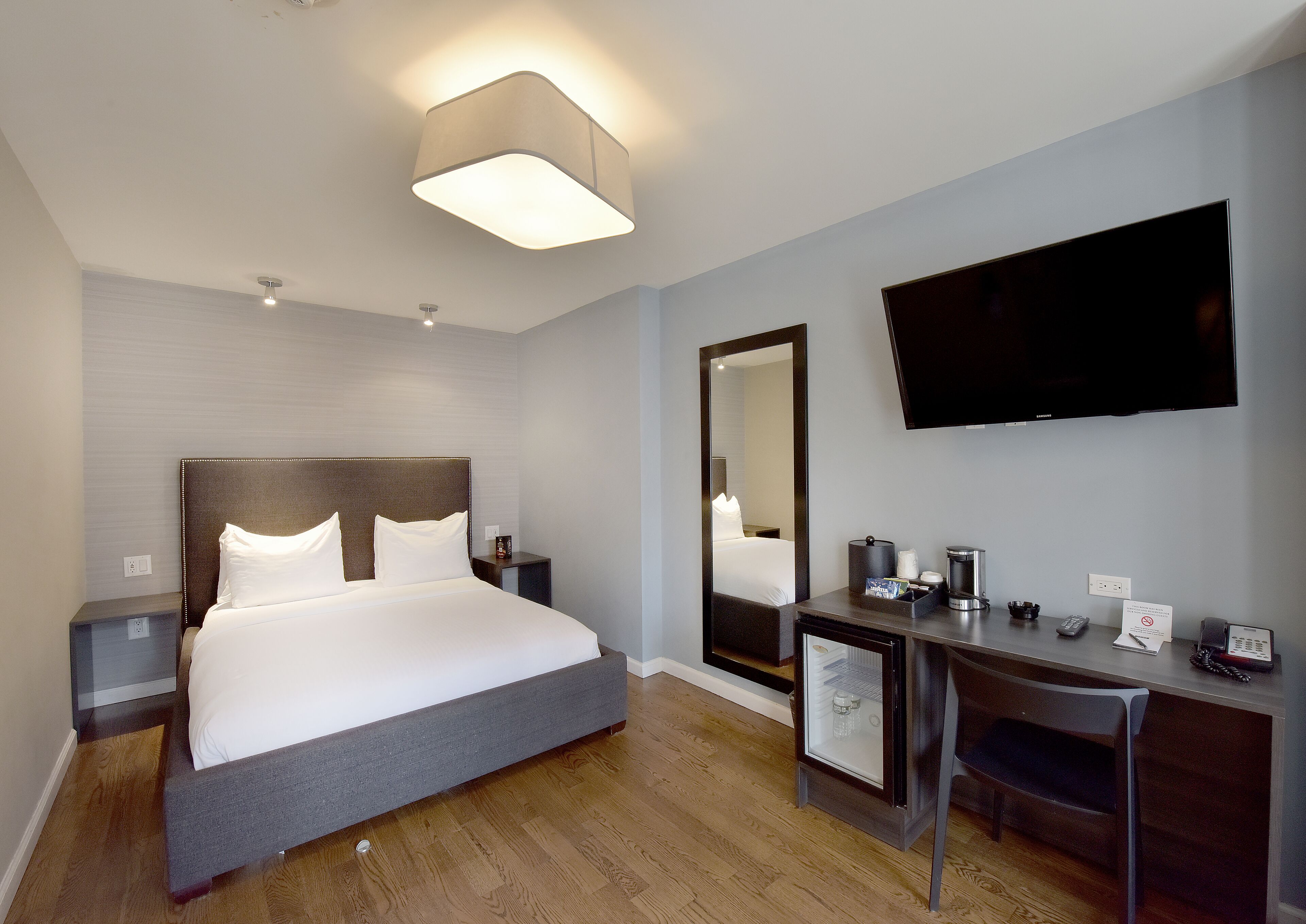Une chambre d’hôtel équipée d’un lit, d’un bureau, d’une chaise, d’une télévision et d’un miroir.