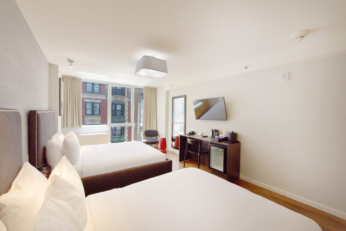 Habitación de hotel con dos camas, un escritorio, una silla, un televisor y una ventana con cortinas.