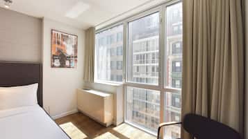 A hotel room with a large window, a bed, a radiator, and a chair.