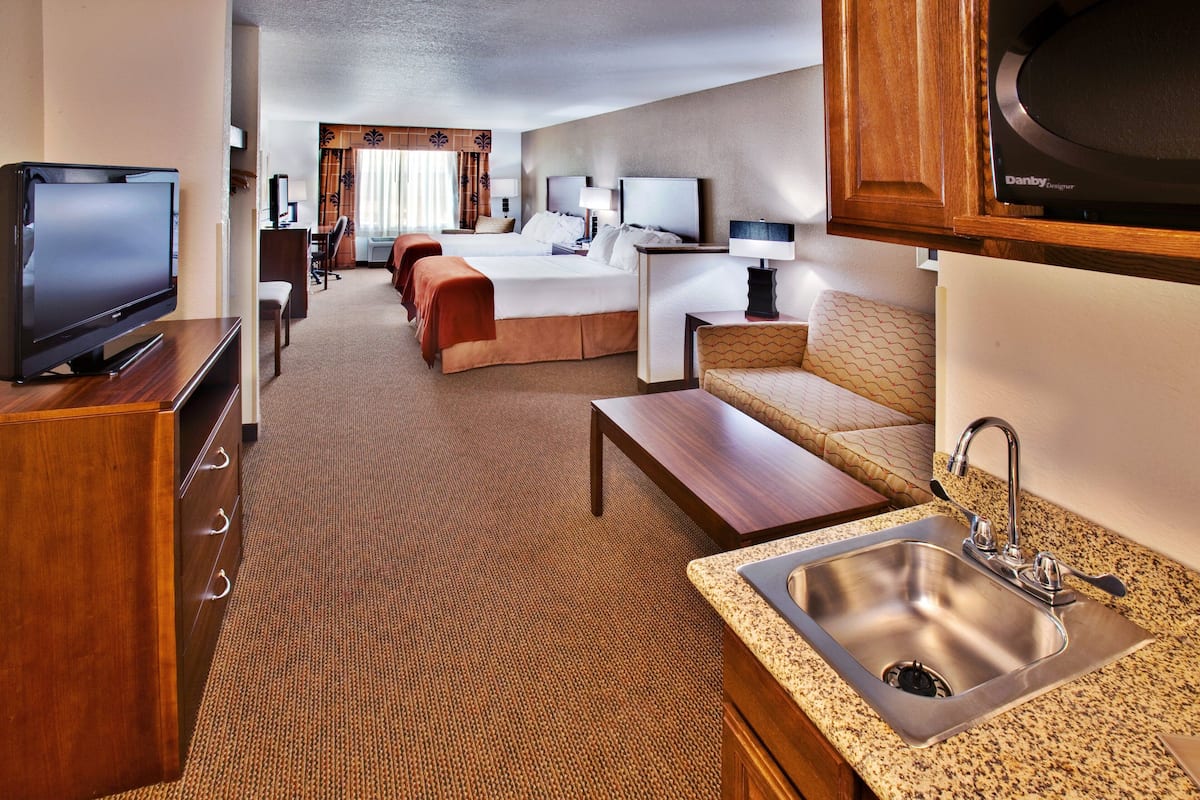 A hotel room with a TV, a bed, a desk, a sofa, and a kitchen area with a sink.