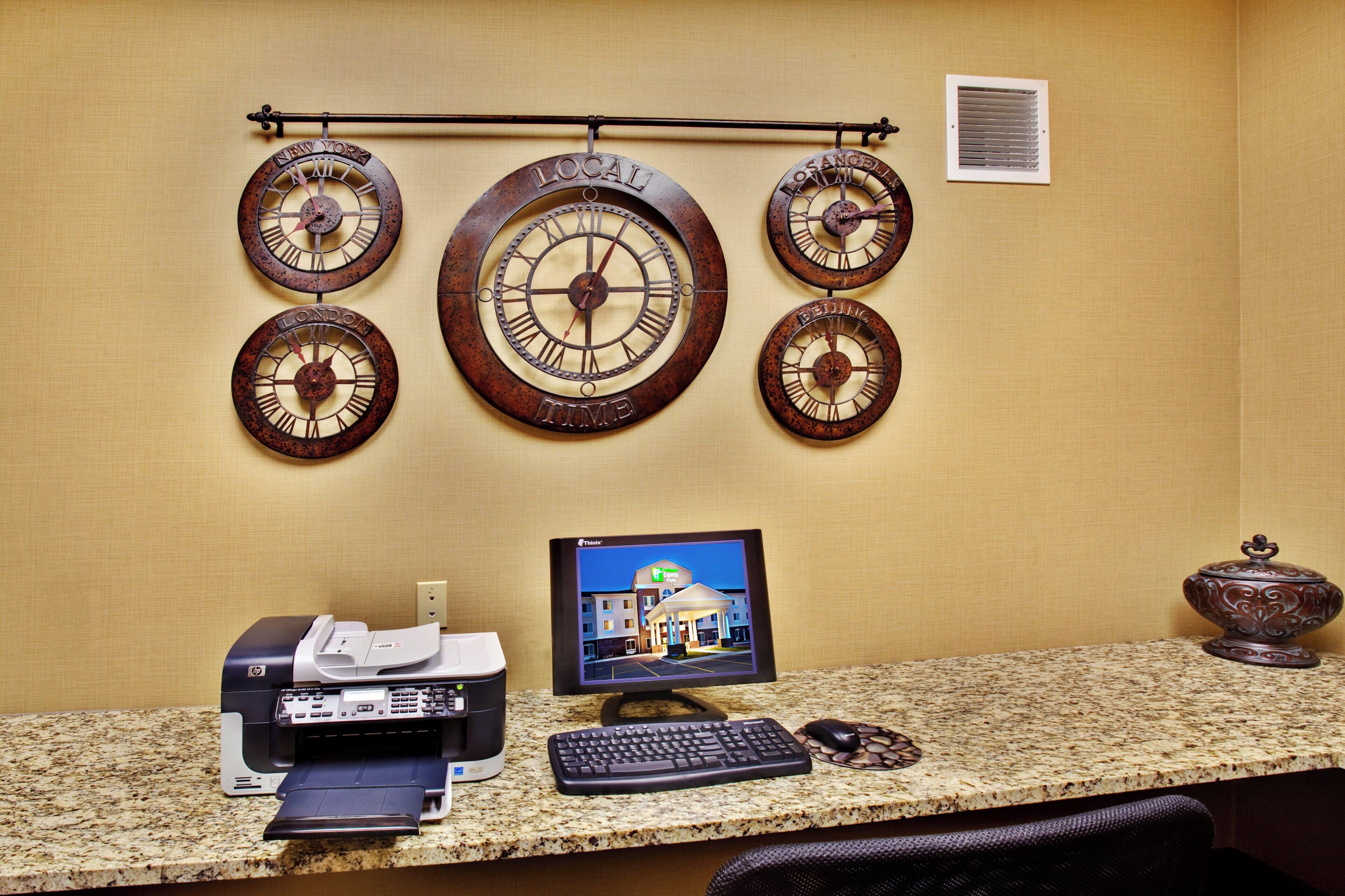 A reception desk with a desktop computer, printer, and a decorative wall clock with city names.