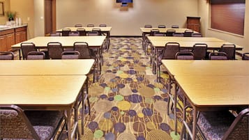 A conference room with multiple tables and chairs, a flat-screen TV mounted on the wall, and a patterned carpet.