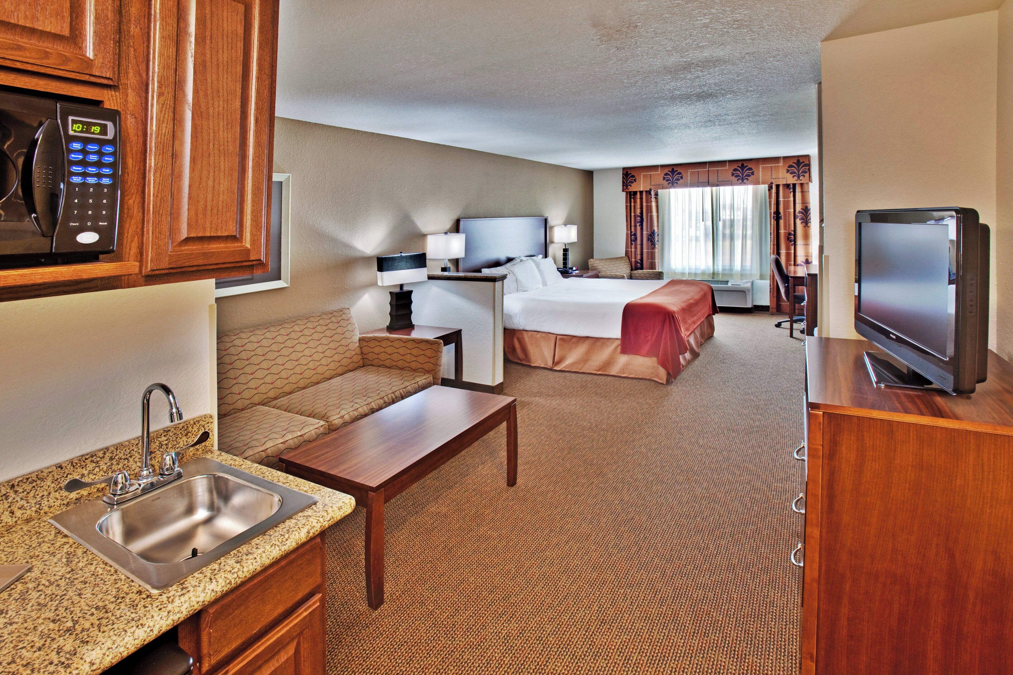 A hotel room with a kitchenette, a bed, a TV, and a seating area.
