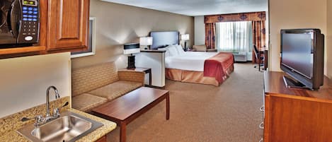 A hotel room with a kitchenette, a bed, a TV, and a seating area.