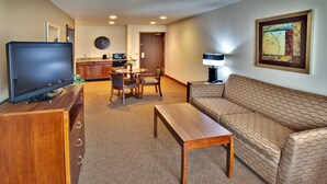 A hotel room with a flat-screen TV, a sofa, a wooden coffee table, a dining table with chairs, a kitchen area, and a clock on the wall. - Holiday Inn Express Hotel & Suites Dubuque by IHG (Dubuque)