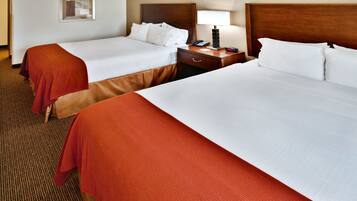 A hotel room with two beds, a nightstand with a lamp, a clock, and a framed picture on the wall.