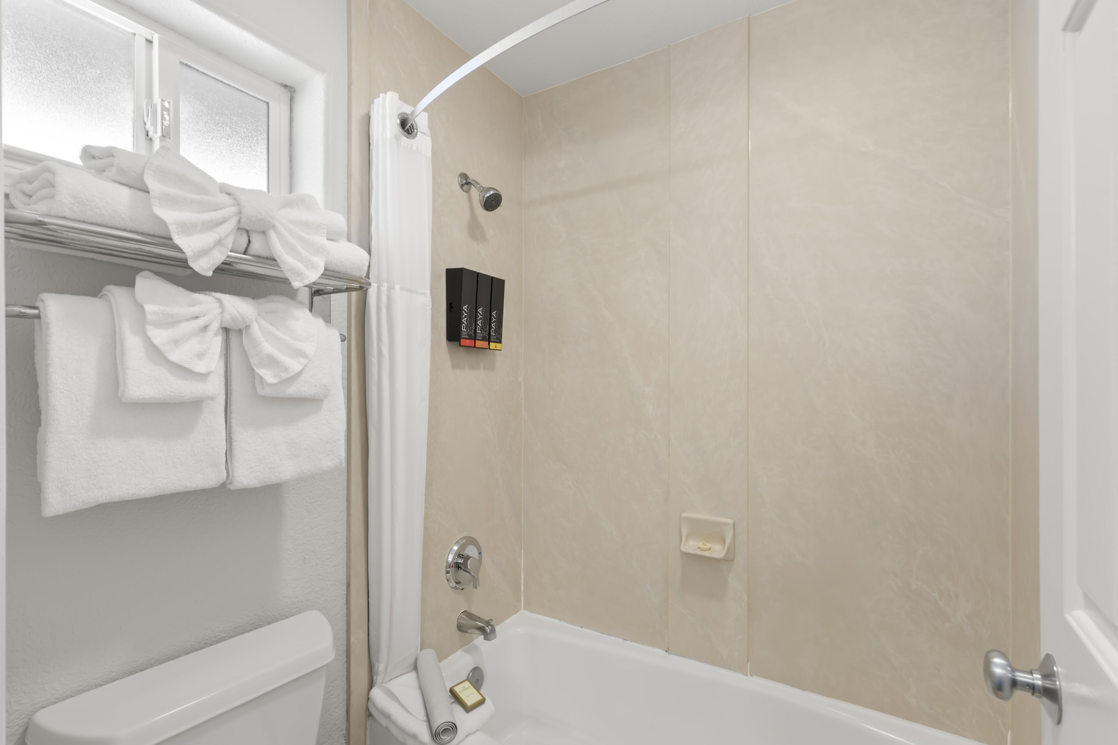 A bathroom with a bathtub, a shower, and a toilet. There are towels on a rack and a soap dish on the wall.
