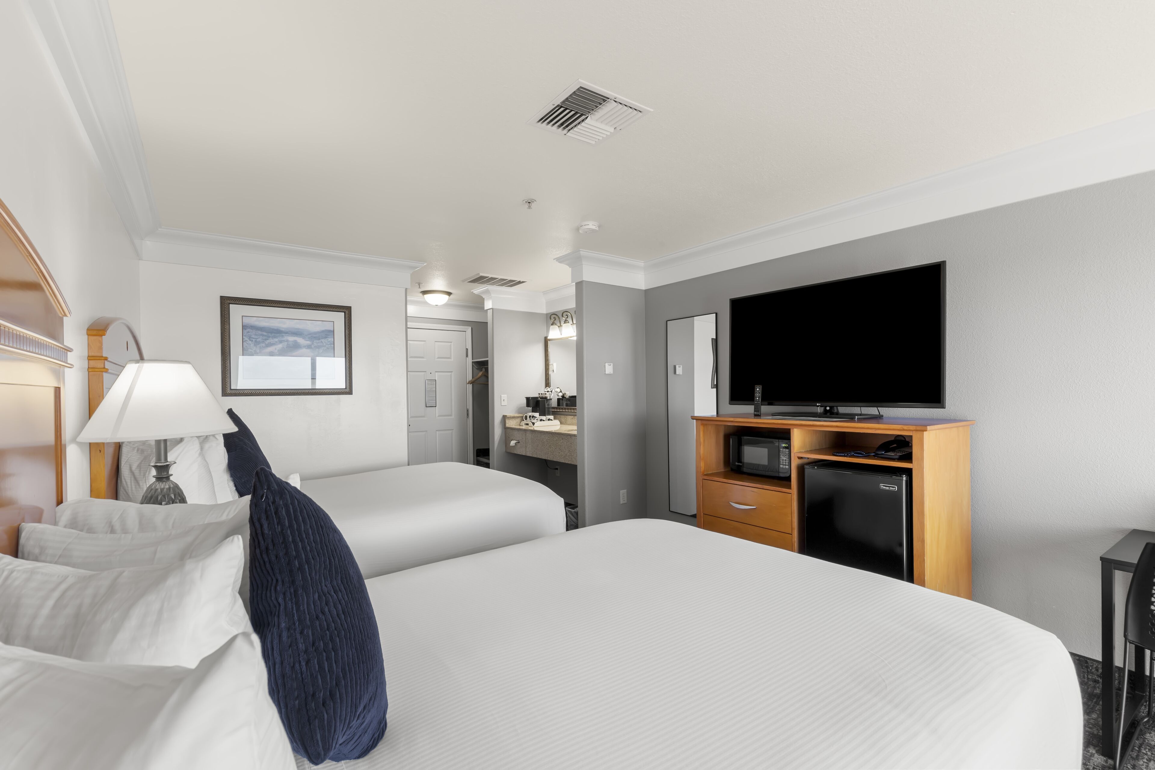 A hotel room with two beds, a TV, a desk with a microwave, and a bathroom in the background.