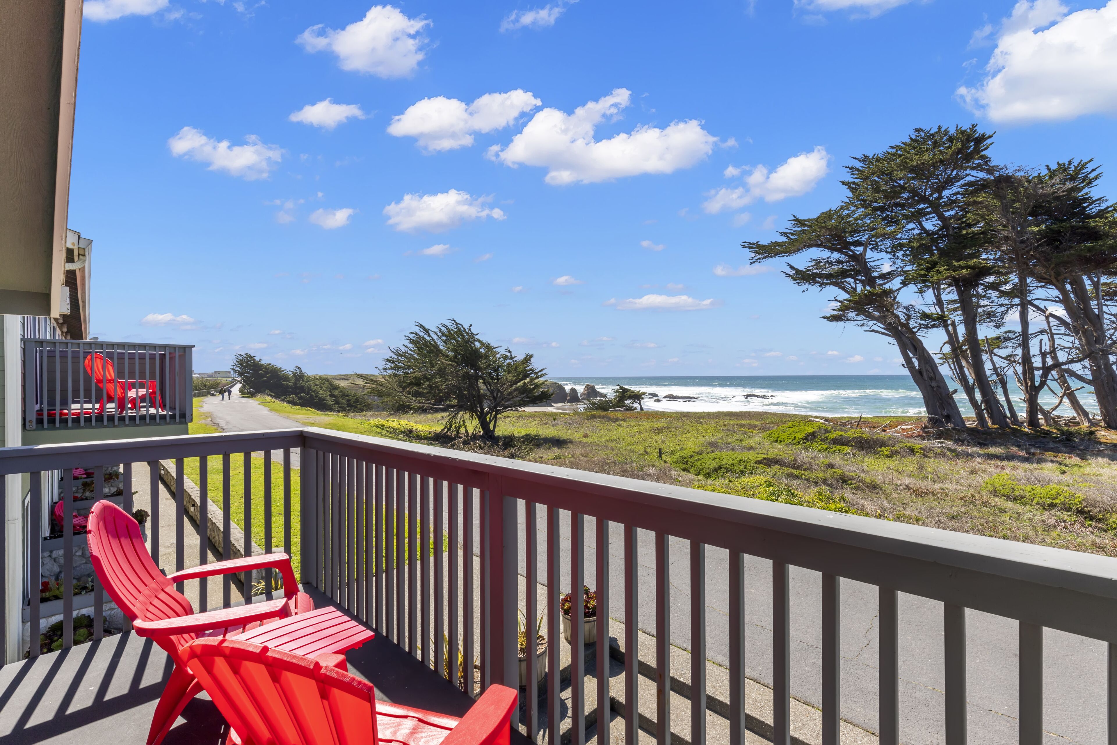 Un balcon avec des chaises rouges donnant sur une plage bordée d’arbres et offrant une vue sur l’océan.