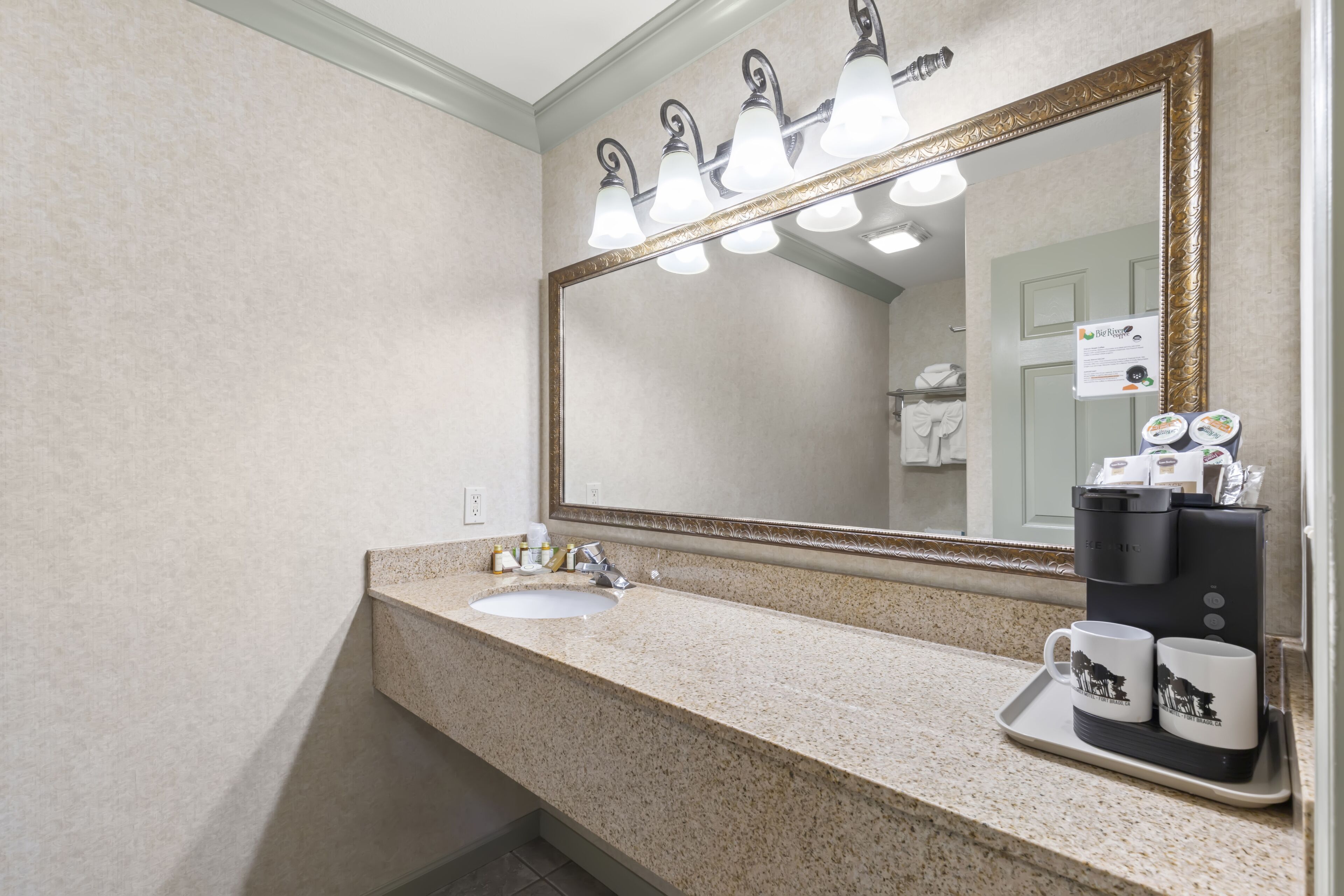 A bathroom with a sink, mirror, and coffee maker.