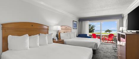 A hotel room with two beds, a desk, a TV, and a balcony with red chairs.