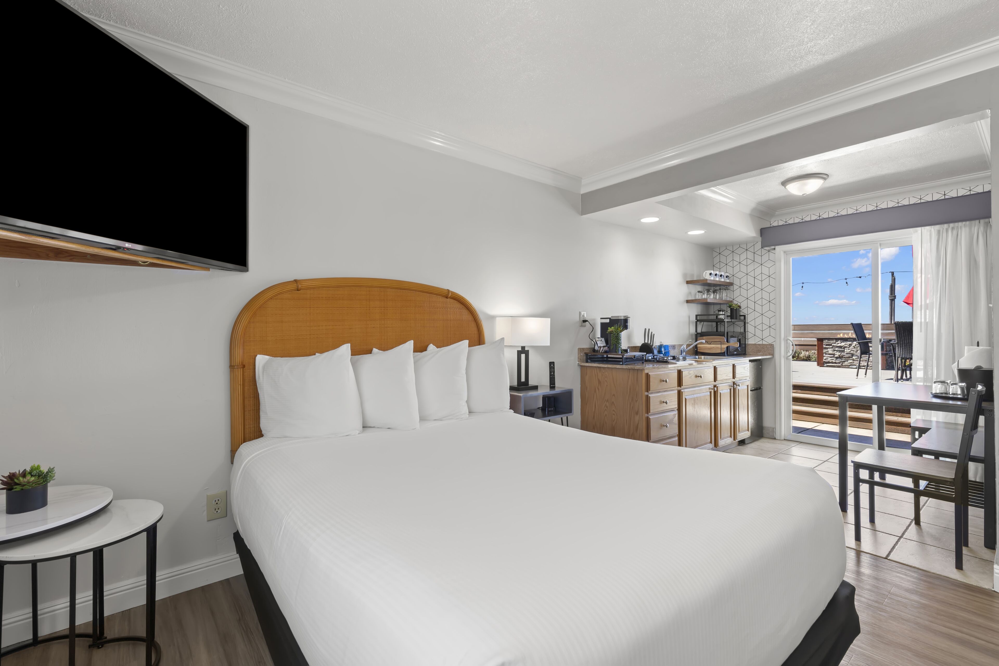 A hotel room with a large bed, a desk, a chair, a TV, and a view of the outside.