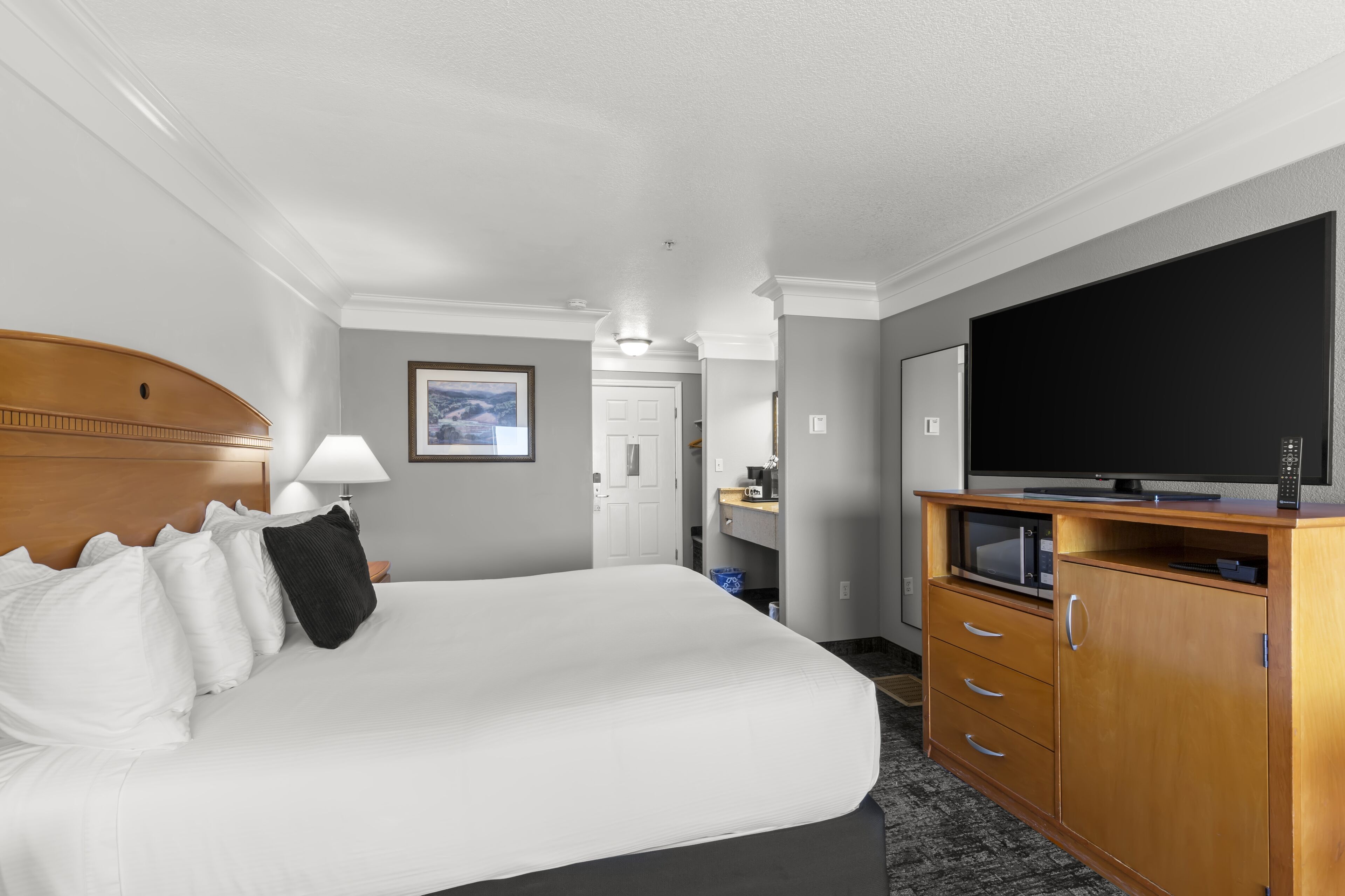 A hotel room with a large bed, a television, a wooden cabinet, and a door leading to a bathroom.