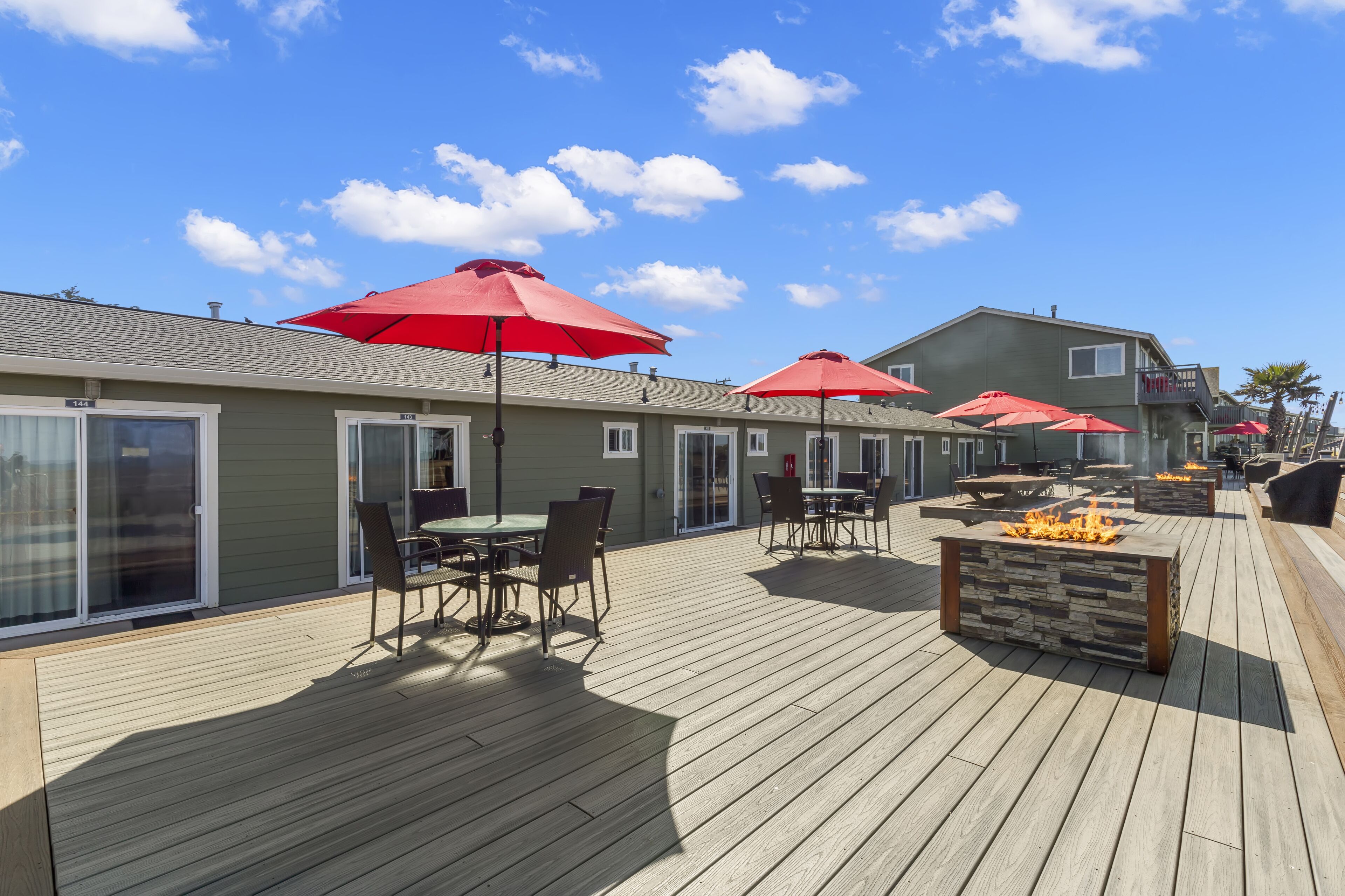 Terraza con mobiliario exterior, sombrillas rojas y una chimenea.