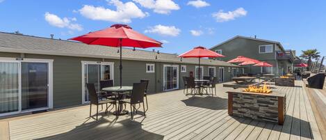 Terraza con mobiliario exterior, sombrillas rojas y una chimenea.