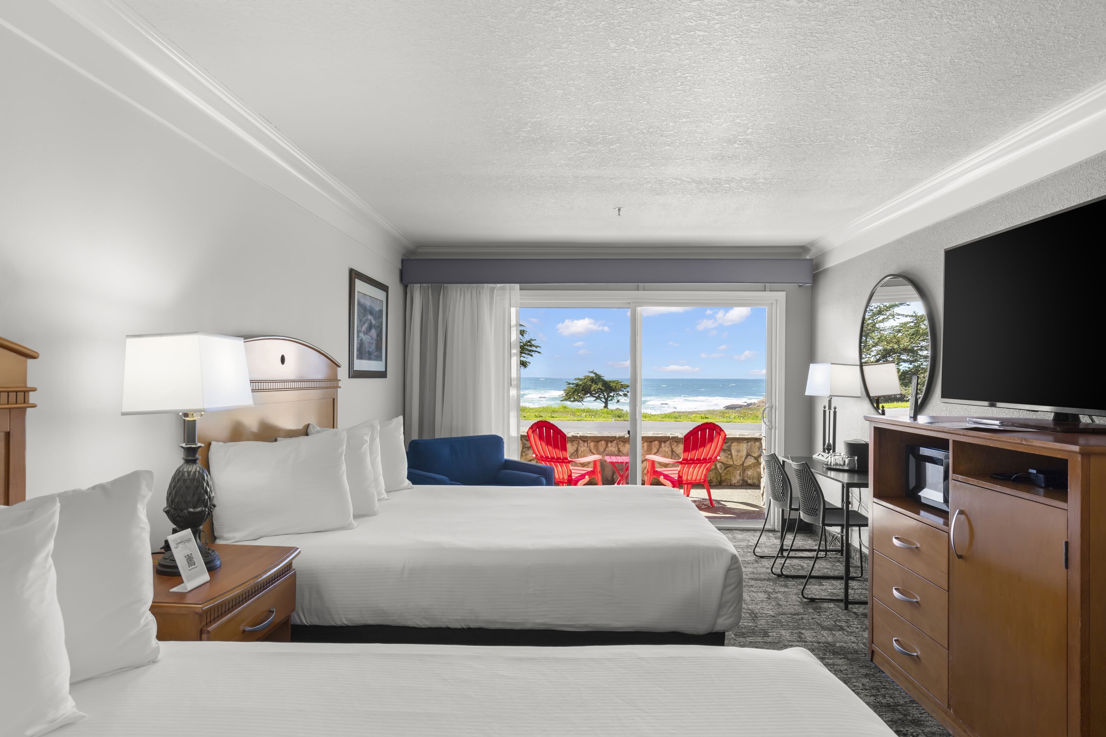 Een hotelkamer met een groot bed, een bureau met een televisie, een stoel en uitzicht op zee.