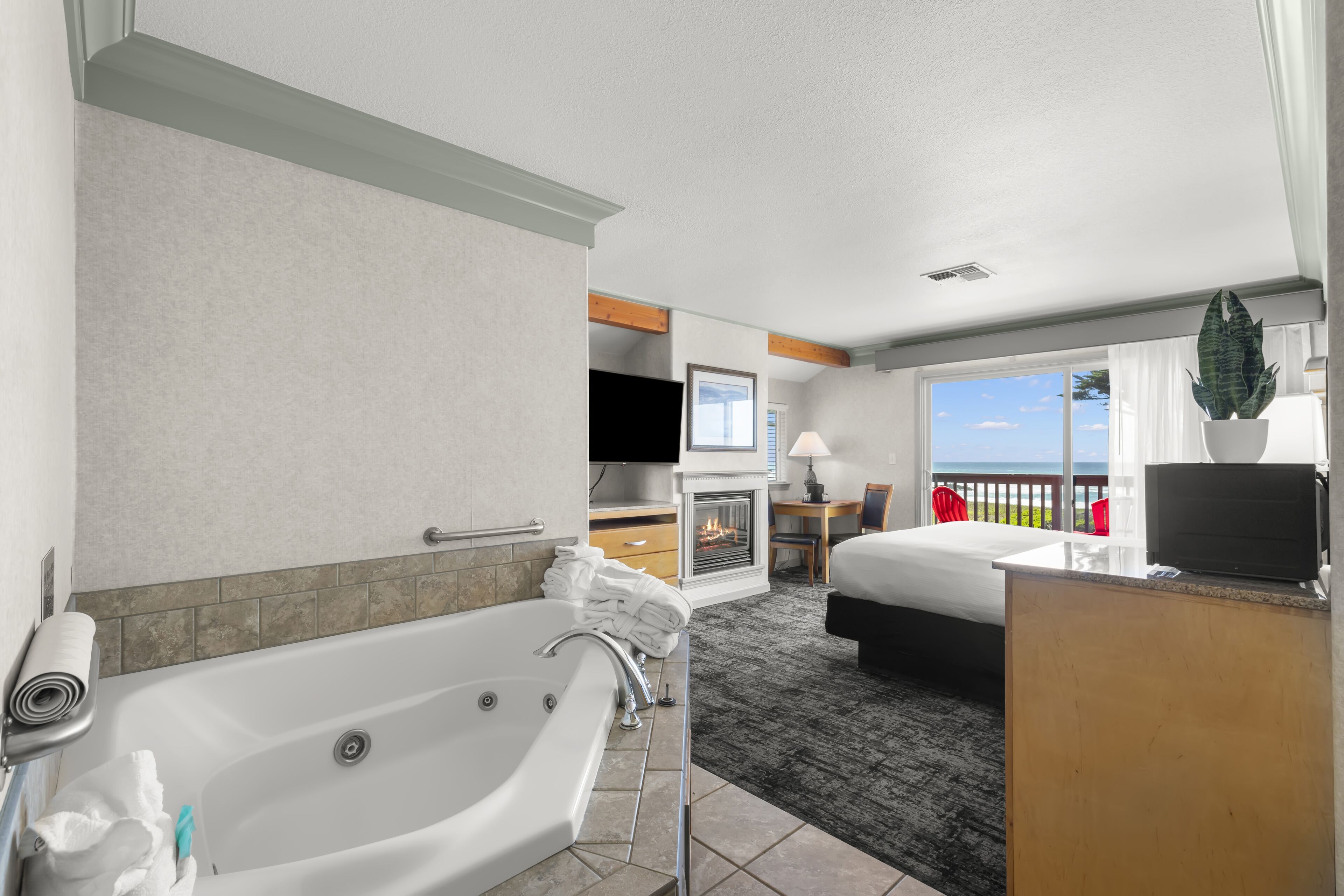 A hotel room with a large bathtub, a bed, a desk with a computer, and a view of the outdoors.