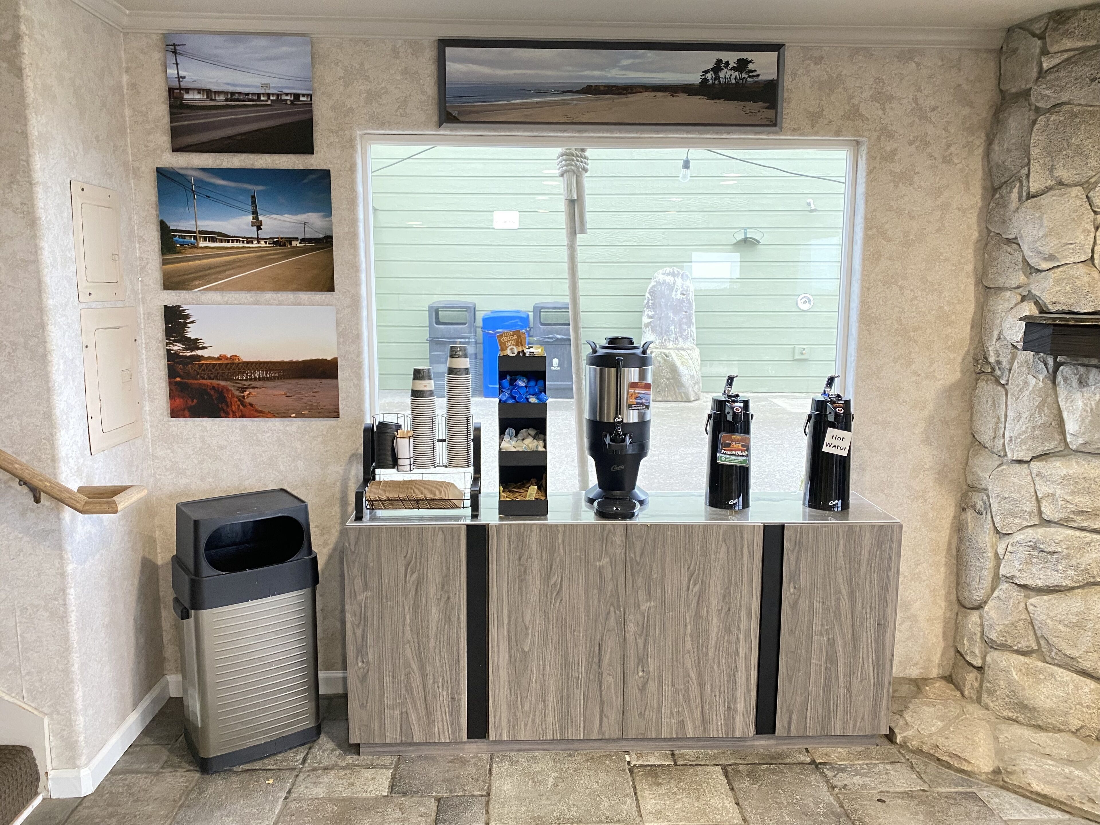 A reception area with a wooden counter, a trash bin, and various amenities including a coffee machine, water dispenser, and a hot water station.