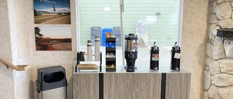 A reception area with a wooden counter, a trash bin, and various amenities including a coffee machine, water dispenser, and a hot water station.