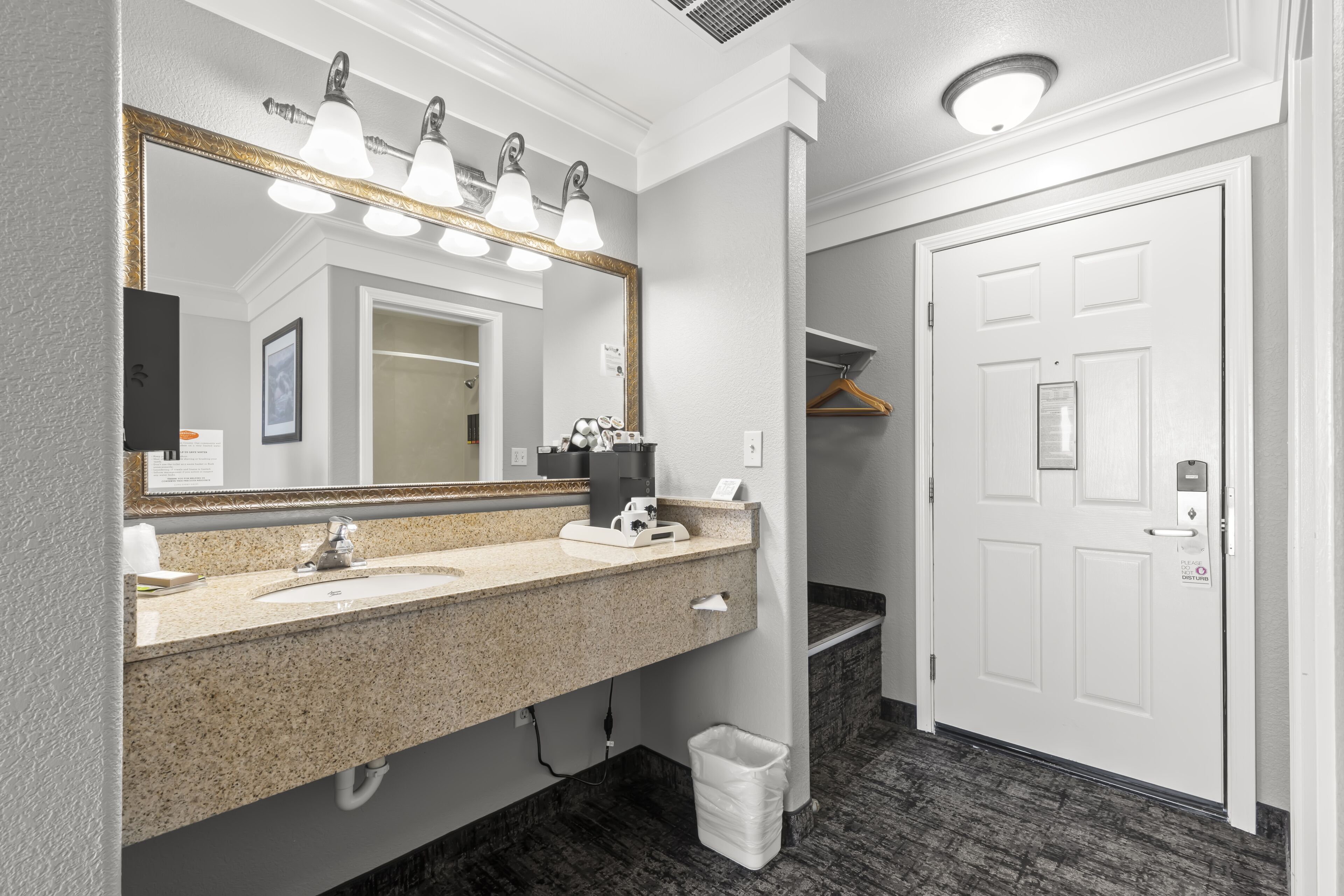 A modern bathroom with a granite countertop, a large mirror, and a white door with a handle.
