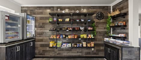 A kitchen with a wooden wall, a clock, and shelves with snacks and beverages.