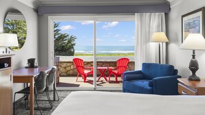 A hotel room with a bed, a desk, a chair, a table, and a view of the ocean through a sliding door.