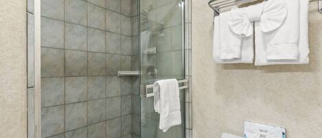A bathroom with a glass shower enclosure, a toilet with a paper towel holder, and a towel rack with folded towels.
