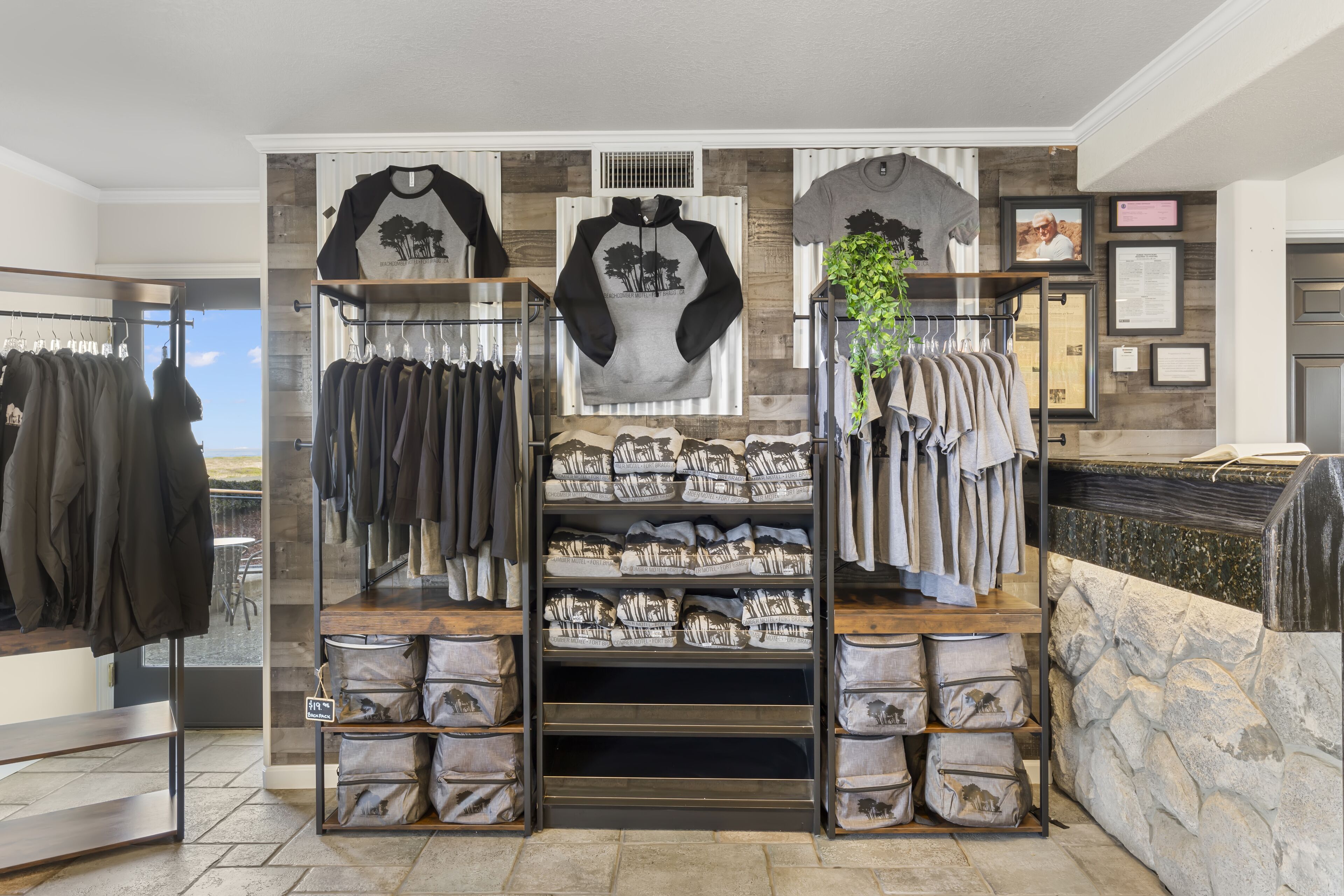 Una tienda de ropa con perchas llenas de prendas, estantes con bolsos y una exposición de camisas.
