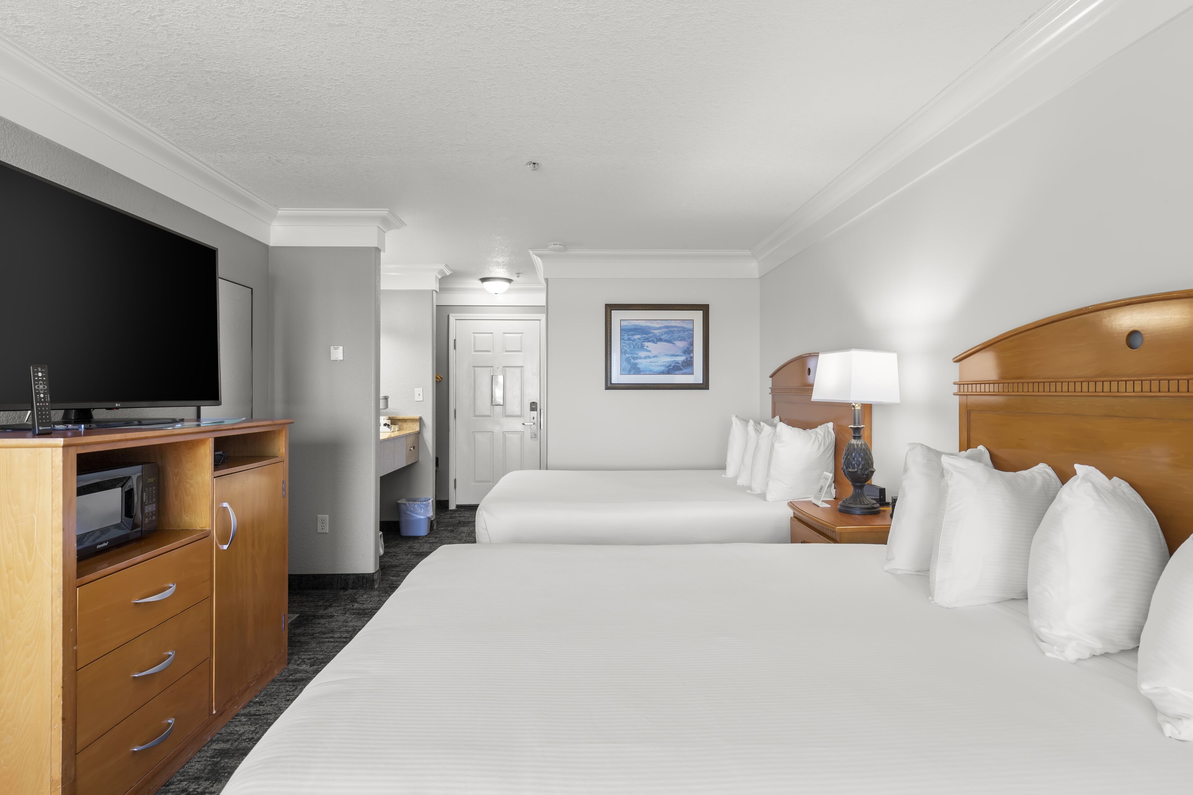 Ein Hotelzimmer mit einem großen Bett, einem Fernseher, einer Holzkommode und einem Nachttisch mit einer Lampe.