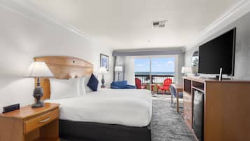 A hotel room with a large bed, a desk, a TV, and a balcony with red chairs.