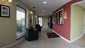 A hallway with a reception desk, a chair, and a potted plant. - Rodeway Inn Shippensburg I-81 (Shippensburg)
