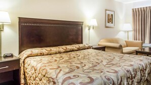 A hotel room with a large bed, a chair, two bedside tables, and two wall-mounted lamps. - Rodeway Inn Shippensburg I-81 (Shippensburg)