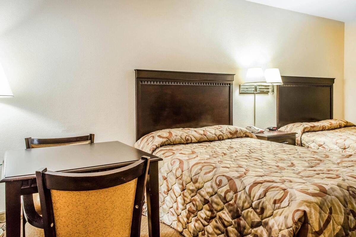 Une chambre d’hôtel comprenant un lit, un bureau, une chaise et une table de chevet avec une lampe.