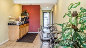A hotel kitchen with a coffee station, a dining area with chairs, and a large potted plant. - Rodeway Inn Shippensburg I-81 (Shippensburg)