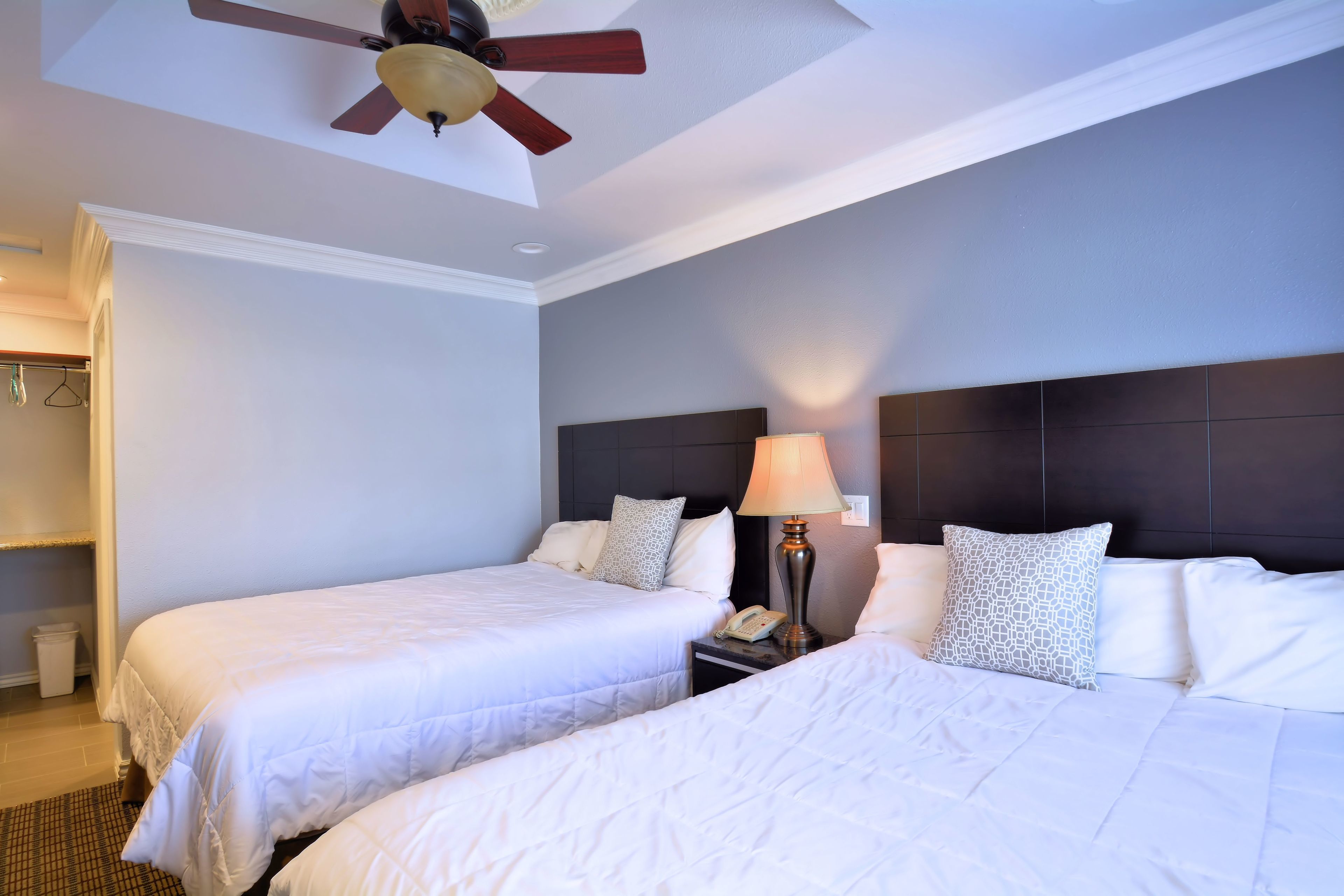 A hotel room with two beds, a ceiling fan, a nightstand with a lamp, and a headboard.