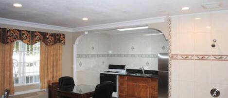 A hotel room with a bed, a desk, a chair, a kitchenette, and a bathroom.