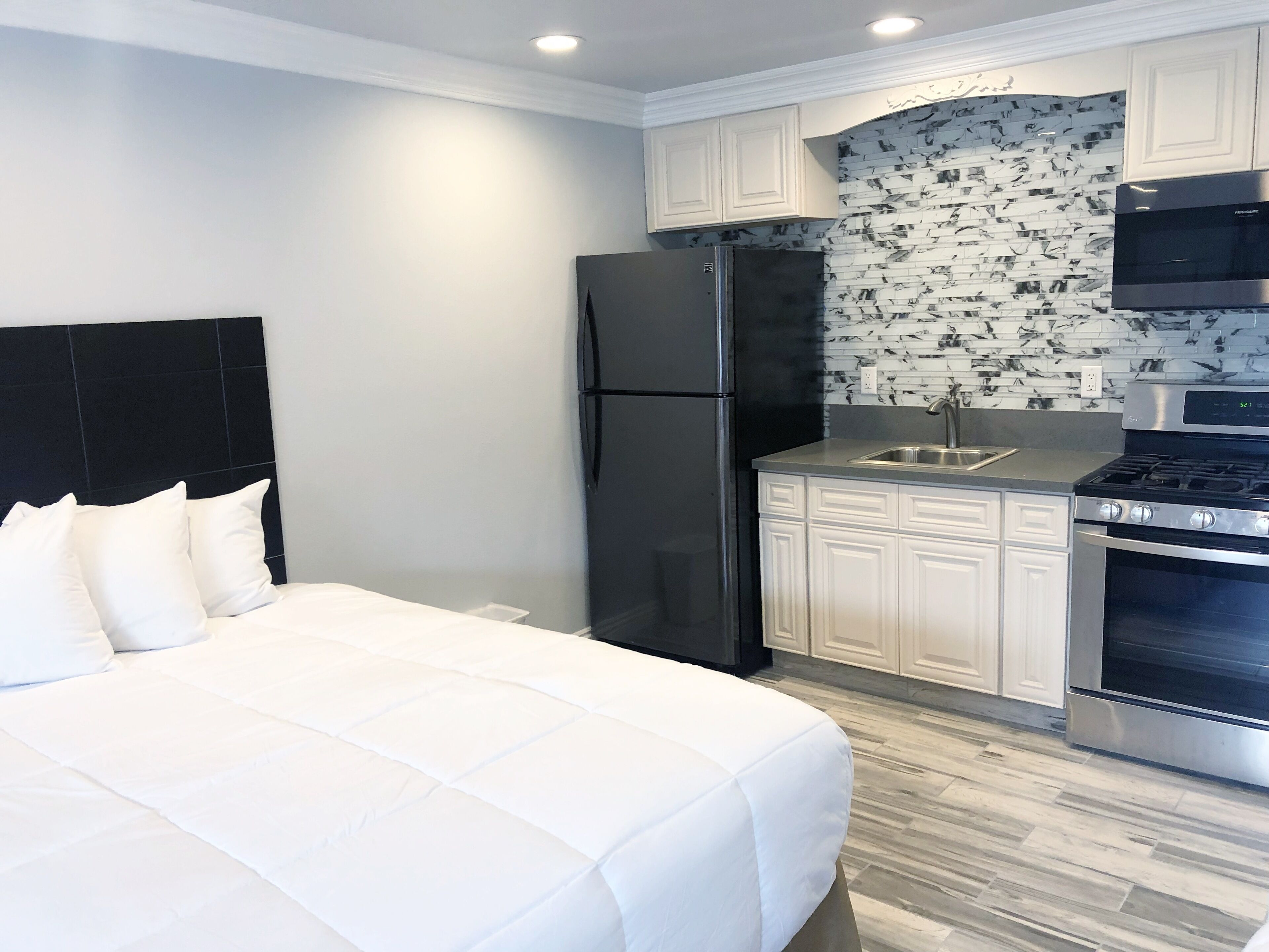 A compact hotel room with a bed, a kitchenette, and a black refrigerator.