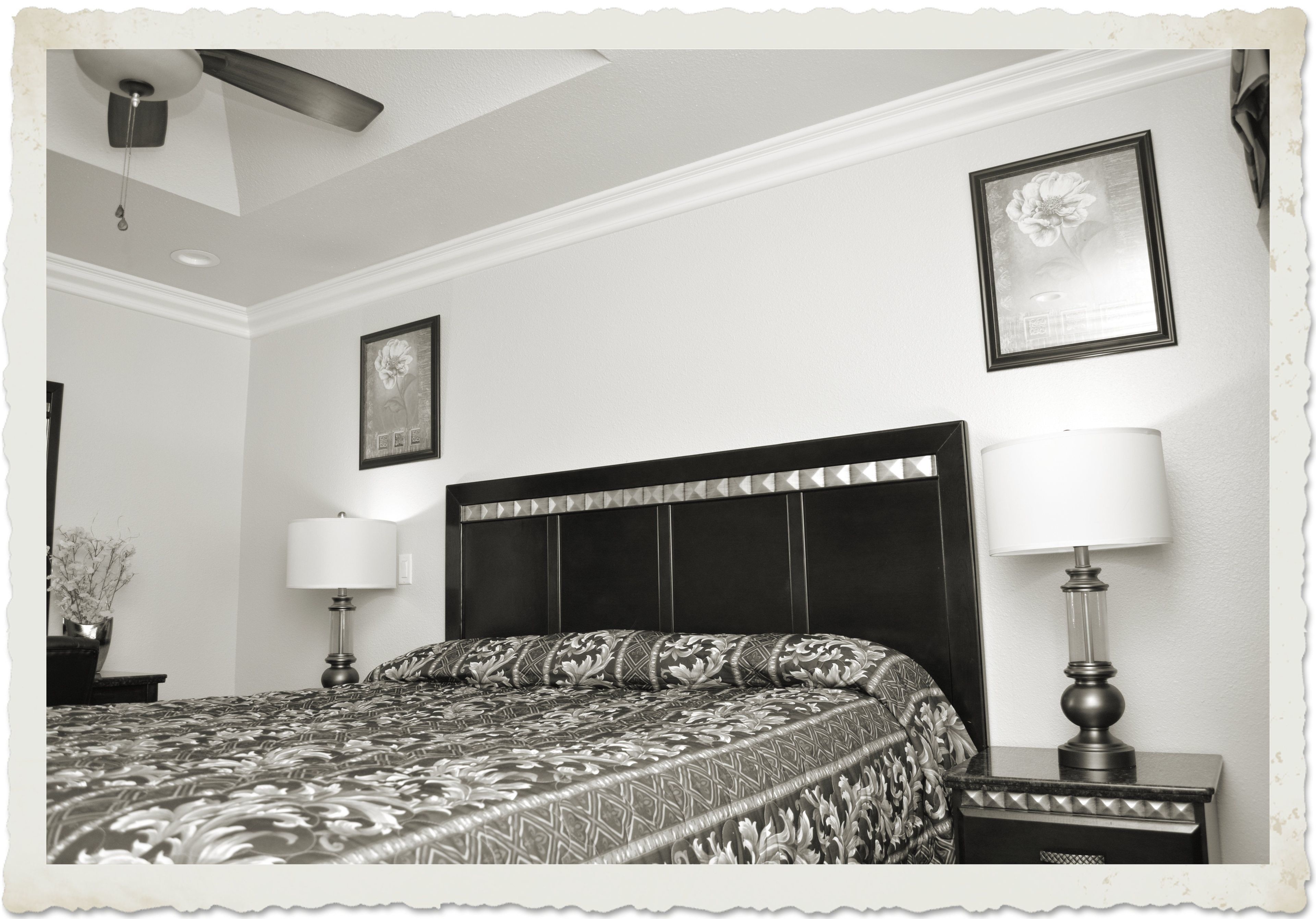 Une chambre à coucher avec un grand lit, deux lampes de chevet, un ventilateur de plafond et des œuvres d’art encadrées accrochées aux murs.