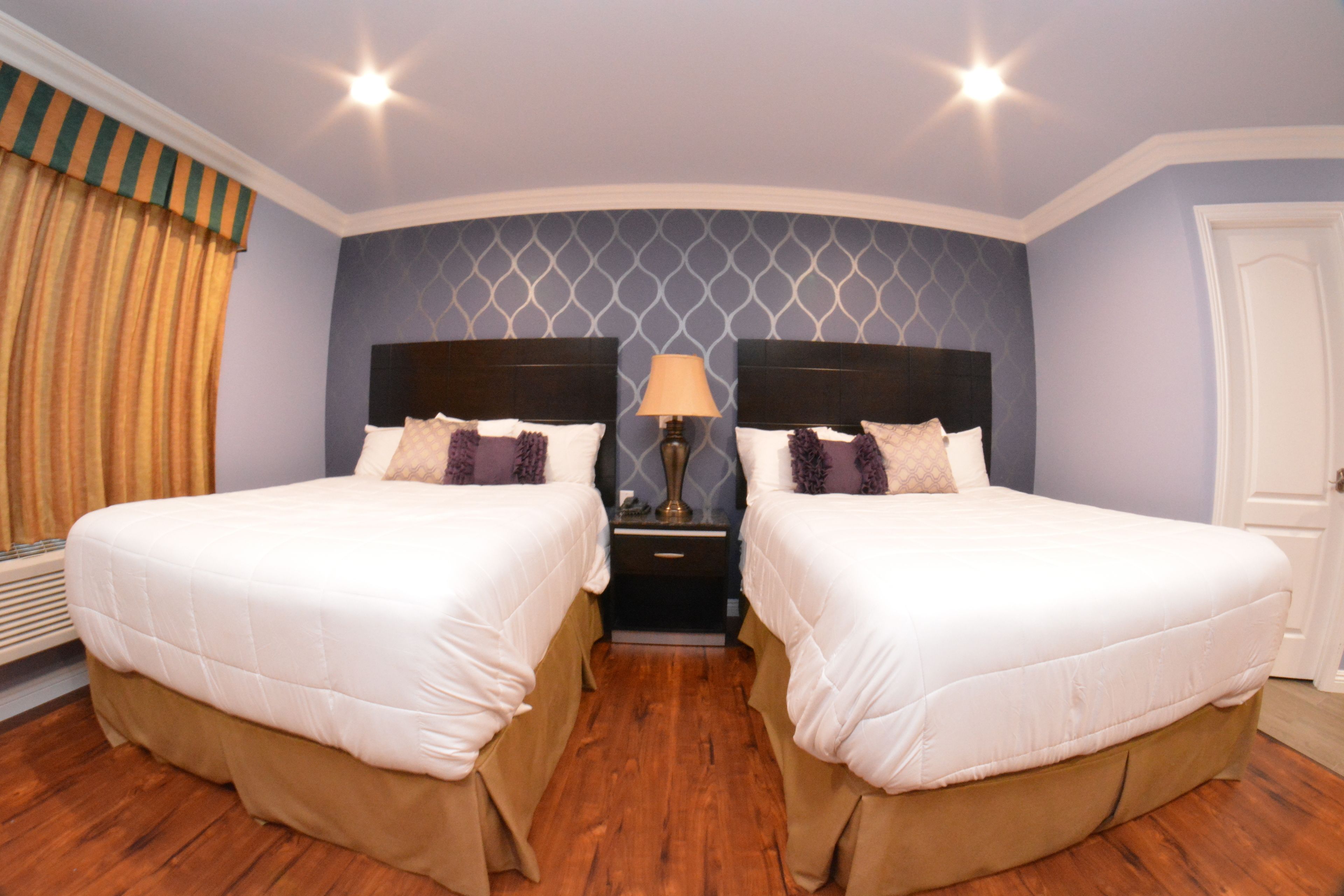 A hotel room with two beds, a nightstand with a lamp, and a patterned wall.