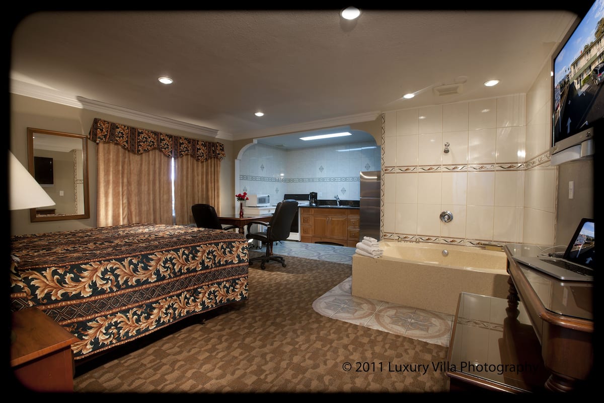 Ein Hotelzimmer mit einem großen Bett, einem Schreibtisch, einem Stuhl, einem Badezimmer mit Badewanne und einem Fernseher.
