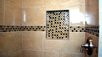 Un baño con azulejos color beige, una pequeña ventana con diseño de rombos y una llave de control de ducha.