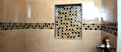 A bathroom with beige tiles, a small window with a diamond pattern, and a shower control valve.
