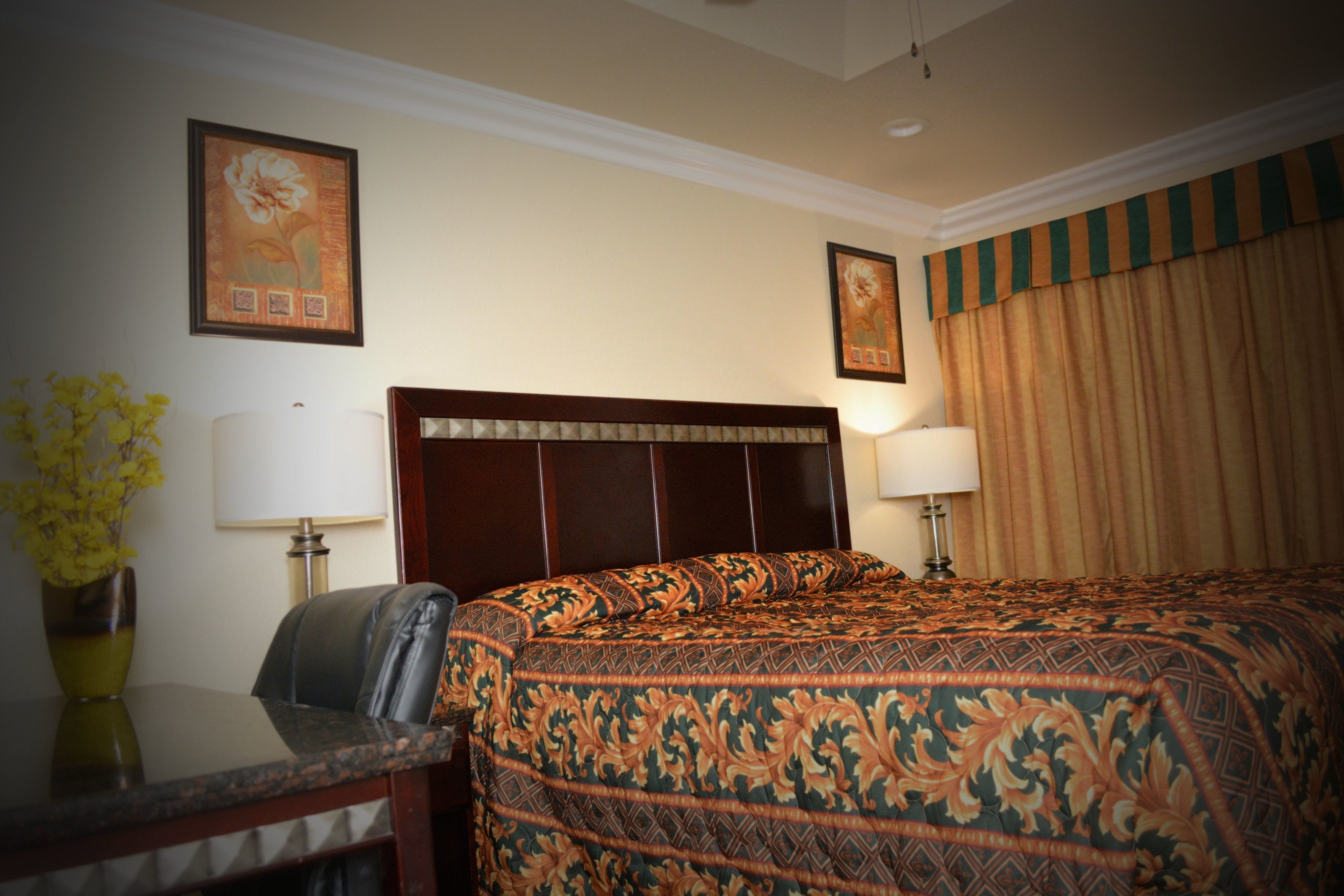 Habitación de hotel con una cama grande, un escritorio con silla, un florero y dos lámparas de pared.