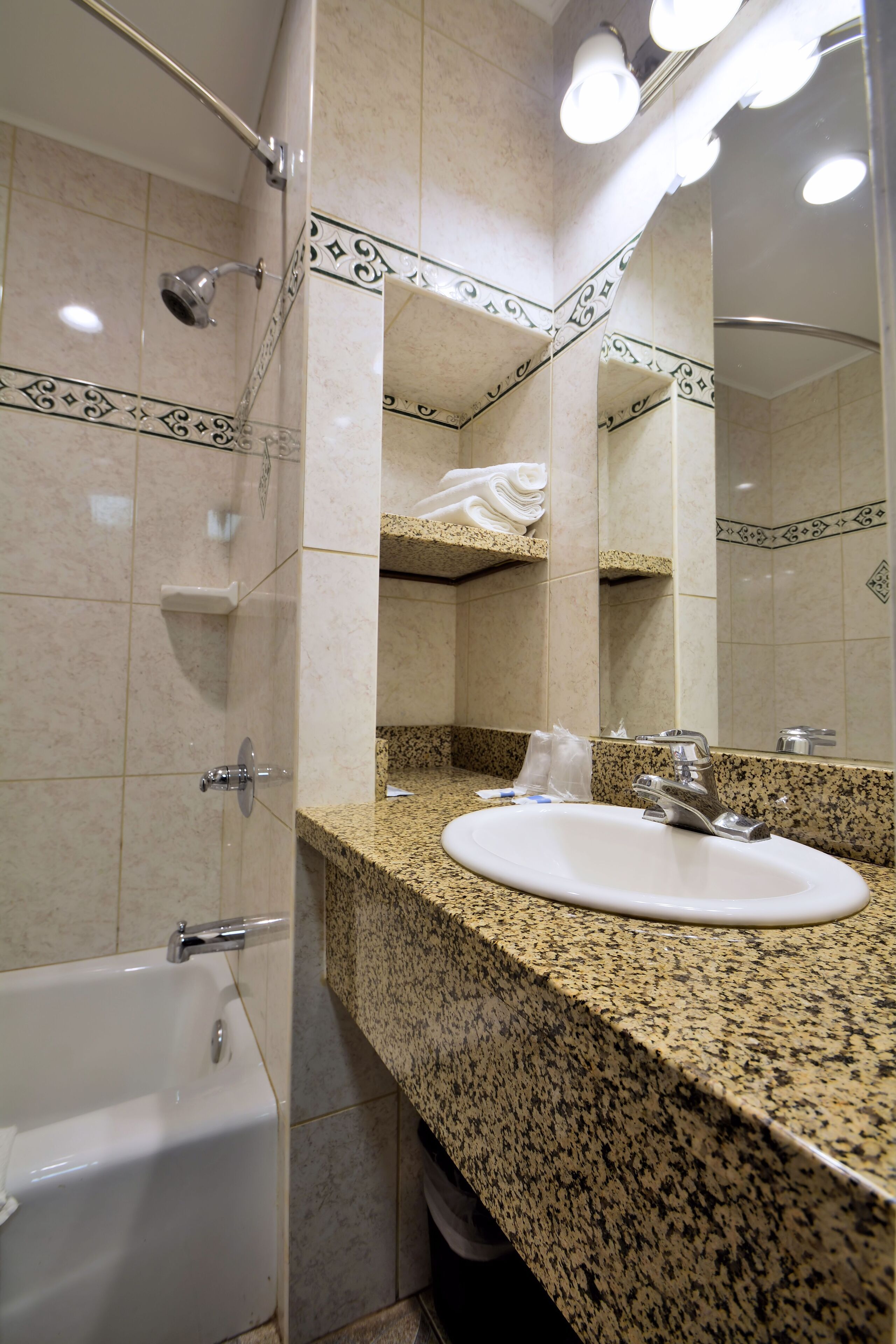 Une salle de bain avec un comptoir en granit, un lavabo blanc, un miroir et une douche.