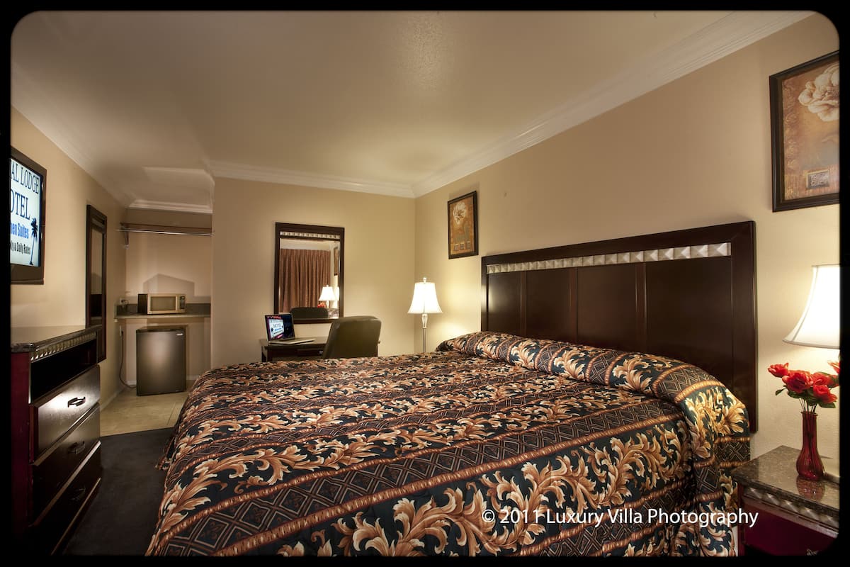 Ein Hotelzimmer mit einem großen Bett, einem Schreibtisch, einem Sessel, einer Mikrowelle und einer kleinen Küchenzeile.
