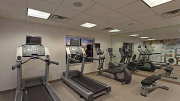 Un gimnasio con cintas de correr, elípticas y una banca.